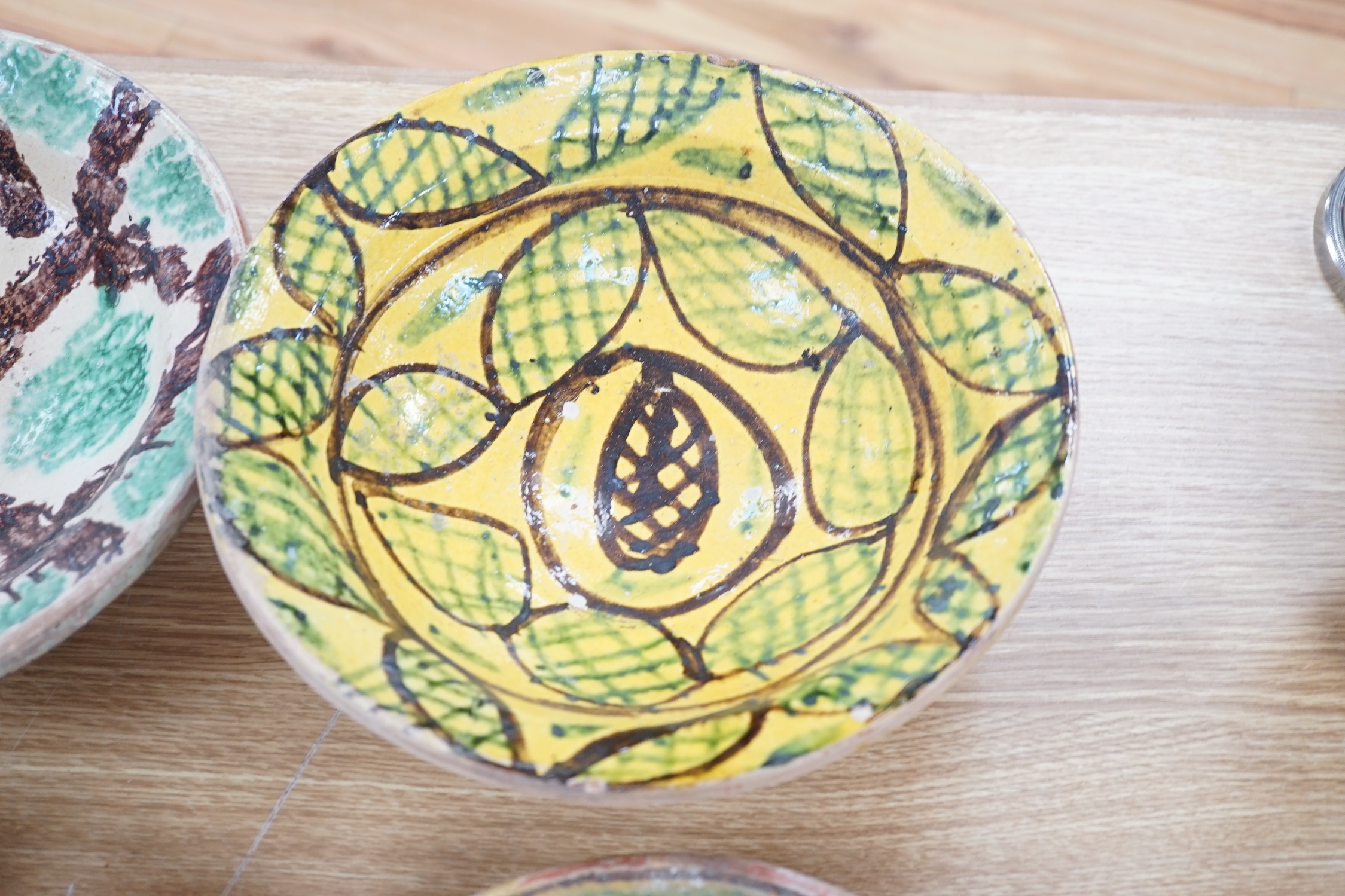 A group of Mediterranean slip decorated pottery dishes, a jar and cover and a bowl, predominantly with yellow and green grounds, the largest 26cm in diameter